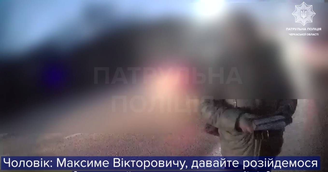 Blurred police video frame from Ukrainian patrol police; bottom caption in Ukrainian with a name.
