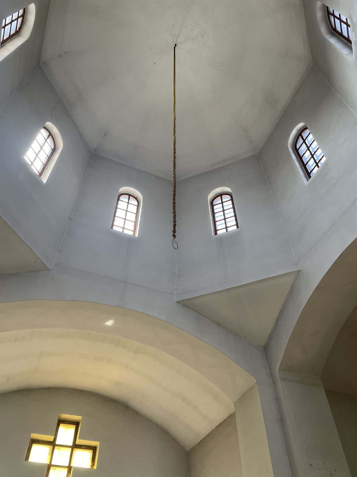 Interior of a church dome with a long hanging chain descending from the ceiling and arched windows around the top.