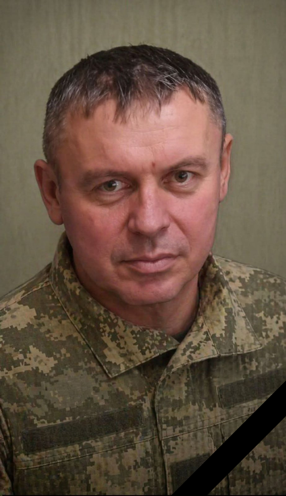 Portrait of a man in camouflage military uniform with a diagonal black mourning ribbon across his chest/torso