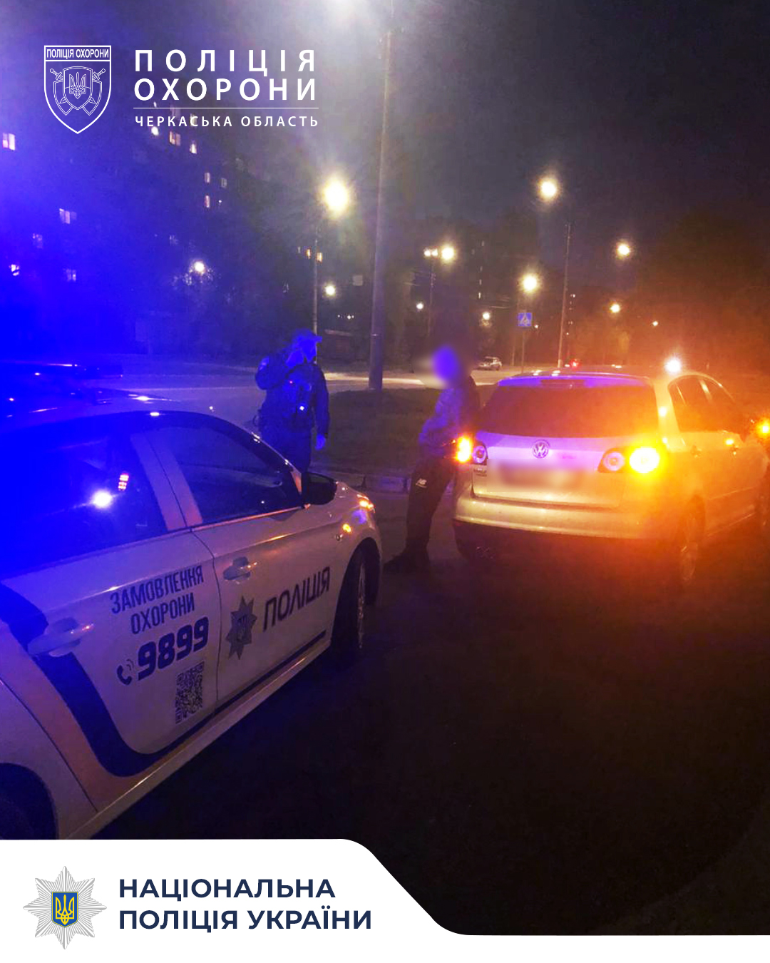 Nighttime scene with two Ukrainian police cars and officers conversing on a dim street, blue and red emergency lights flashing.