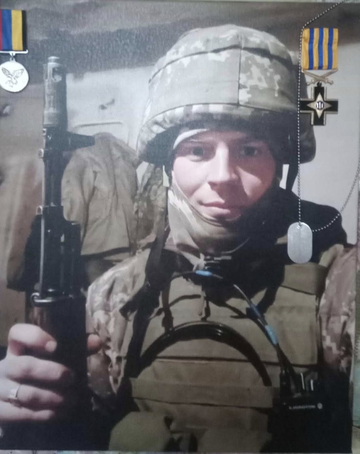 Soldier in camouflage gear wearing a helmet, gripping a rifle, with dog tags visible nearby.