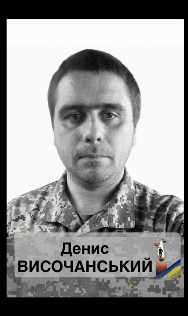 Portrait of a man in camouflage uniform with a banner across his chest reading Денис ВИСОЧАНСЬКИЙ.