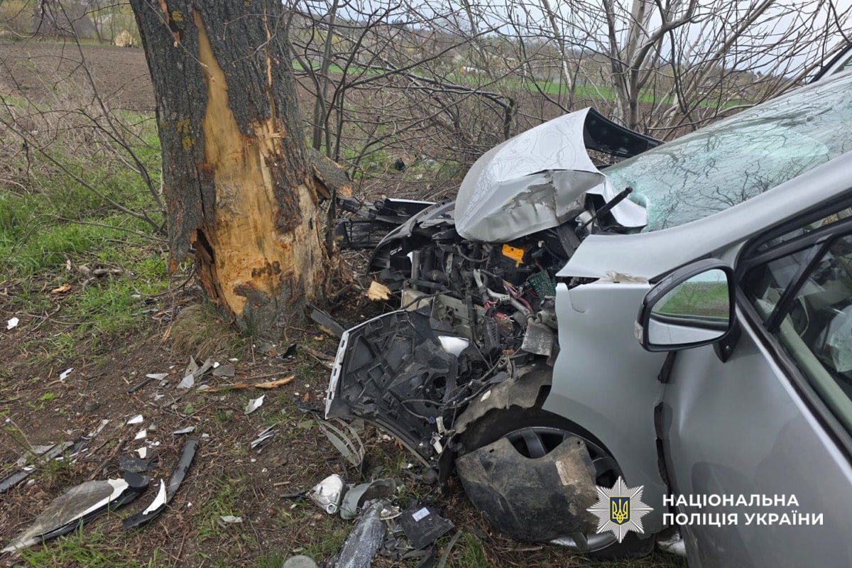 Car crashed into a tree with heavy front-end damage; debris scattered on the ground and a damaged windshield visible. (Ukrainian police watermark)