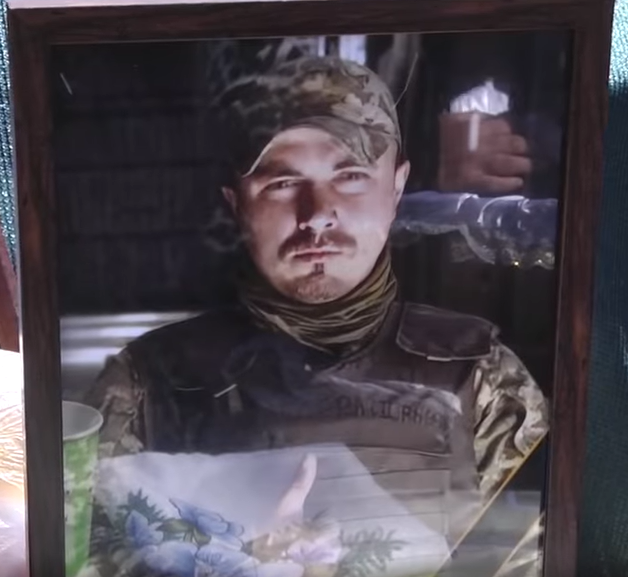 Framed portrait of a man in camouflage cap and tactical vest, looking to the side.