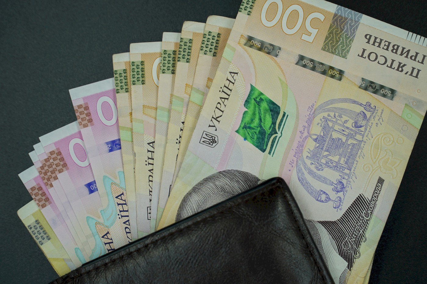 Fanned Ukrainian hryvnia banknotes partially tucked into a black leather wallet.