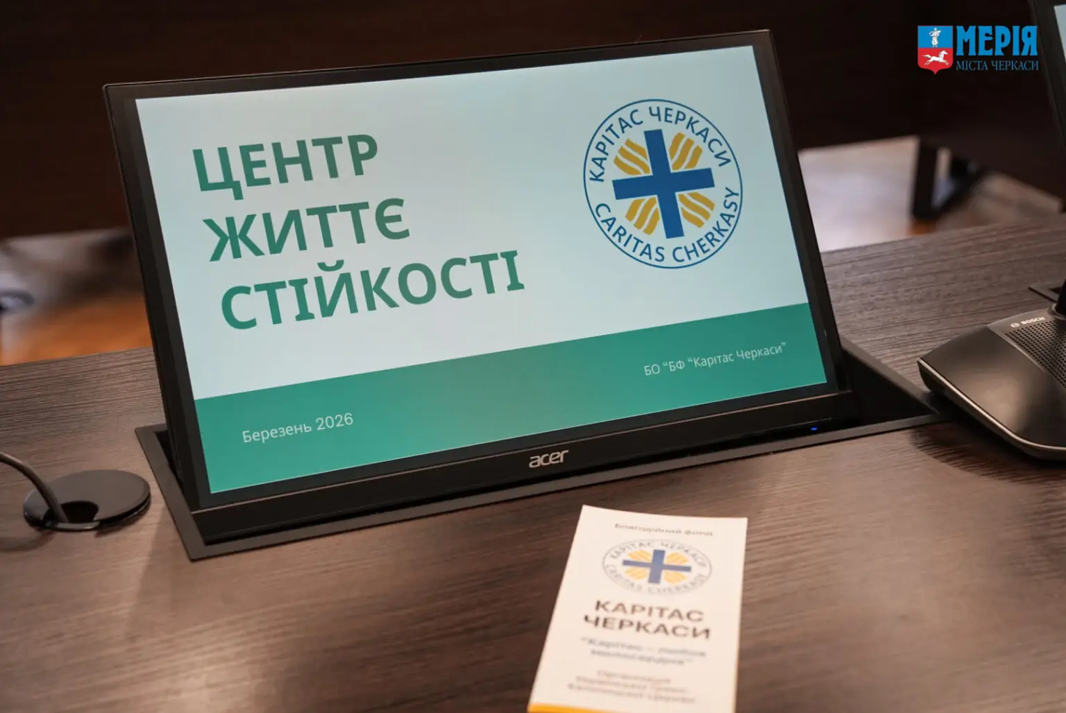 Laptop screen displaying a presentation slide with Ukrainian text and the Karitas Cherkasy logo; a brochure sits on the desk nearby, and a 'Media' badge is in the top-right corner.