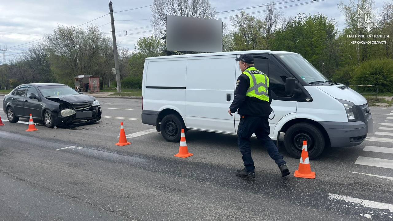 Traffic police officer in a high-visibility vest at a road collision involving a white van and a damaged black car, orange cones placed around the scene.