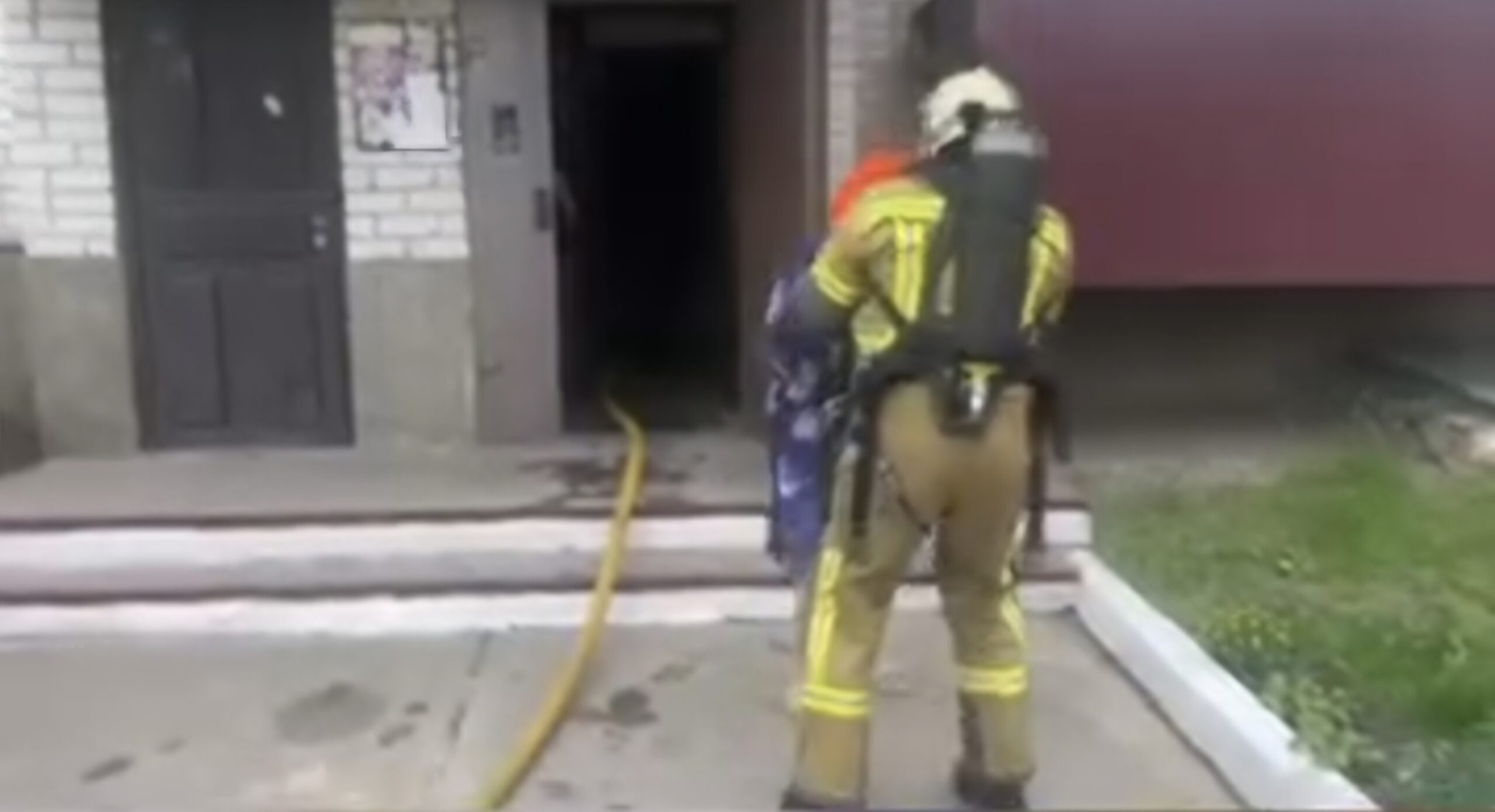 Firefighter in yellow turnout gear handling a hose outside a doorway of a building.