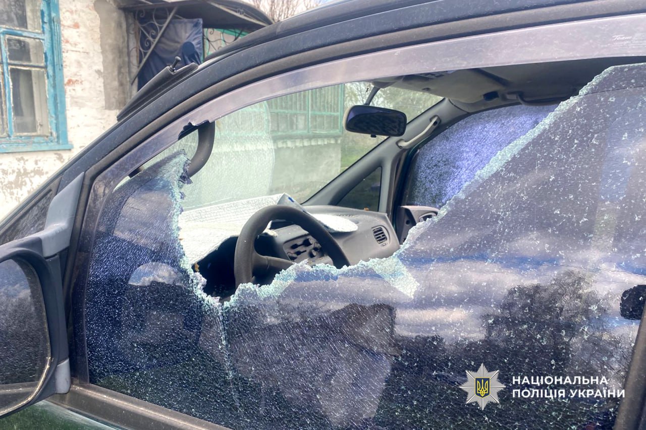 Damaged car with a shattered front window; interior steering wheel visible, police emblem in corner (Ukraine).