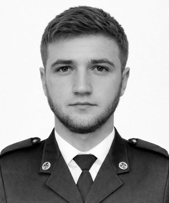 Young man in a formal uniform facing the camera; neutral expression, short hair, trimmed beard.