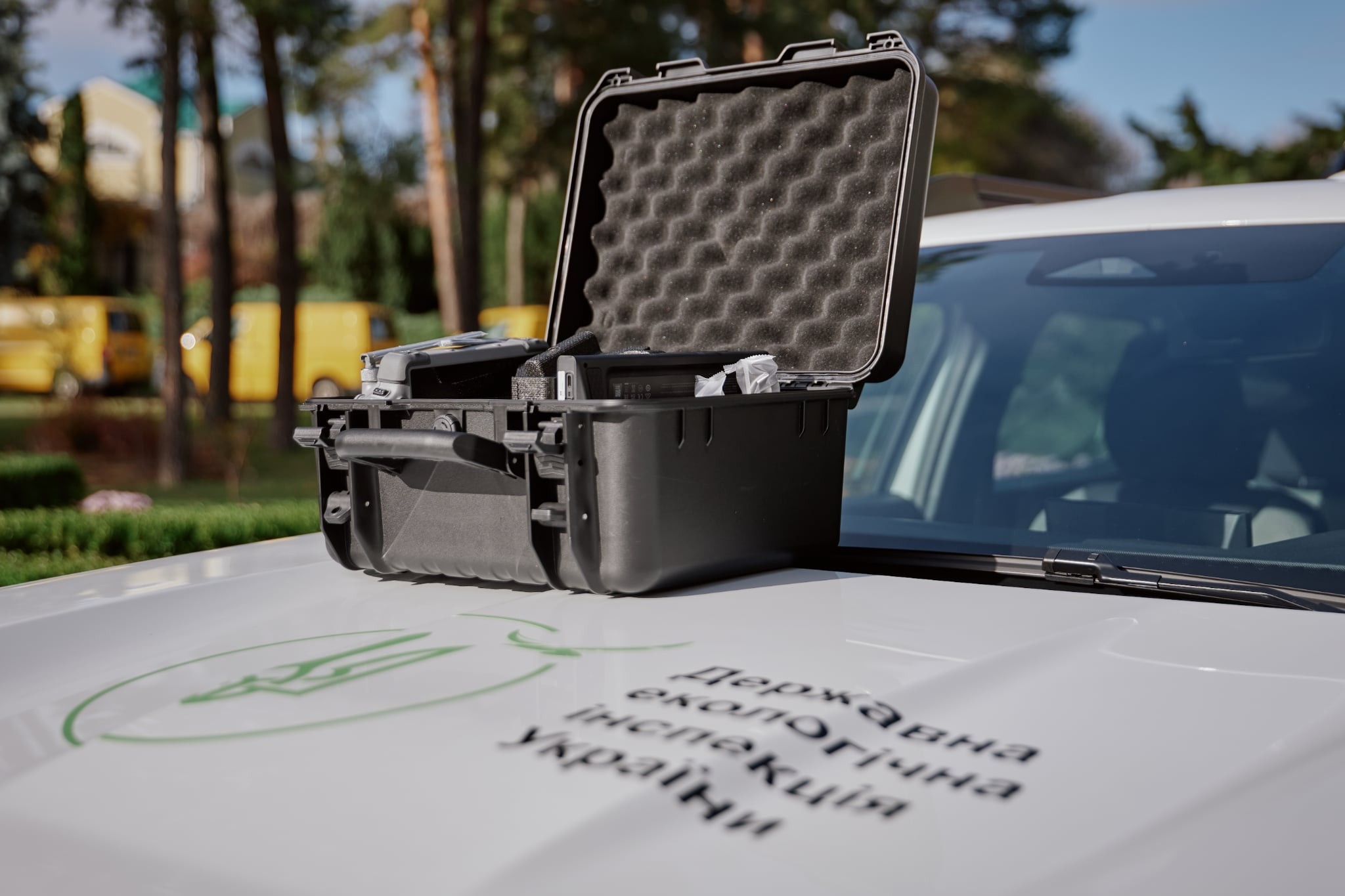 Open hard case with egg-crate foam insert resting on a car hood in an outdoor parking area, gear visible inside the case.