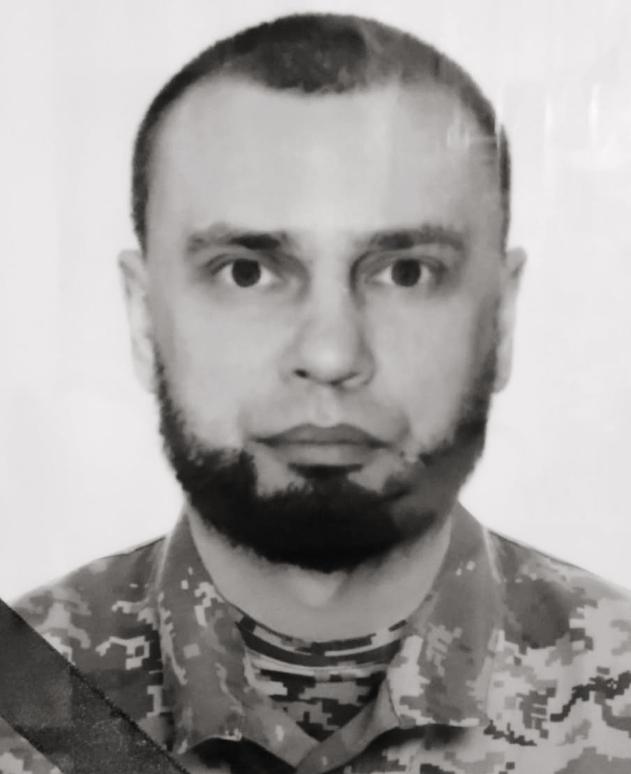 Close-up portrait of a man with a beard in camouflage military uniform awaiting instruction at the camera angle.