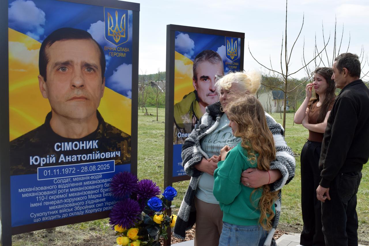 Family pays respects at a memorial with two large soldier portraits and Ukrainian colors.