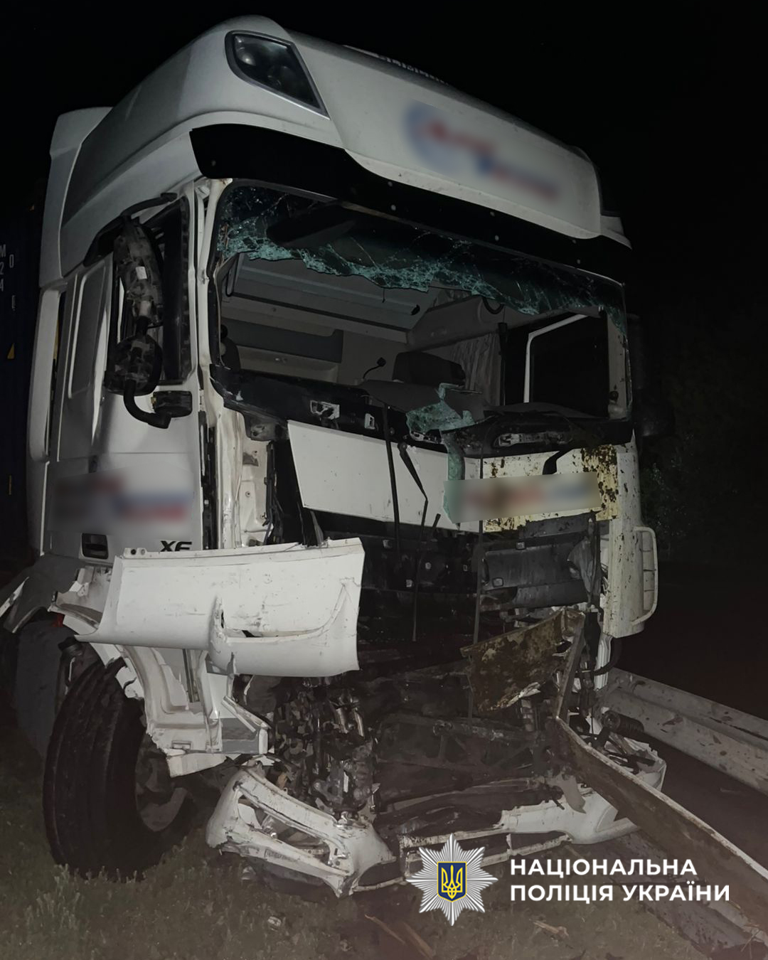White semi-truck with severe front-end damage crashed into a guard rail at night; shattered windshield and twisted bumper, Ukrainian police watermark visible.