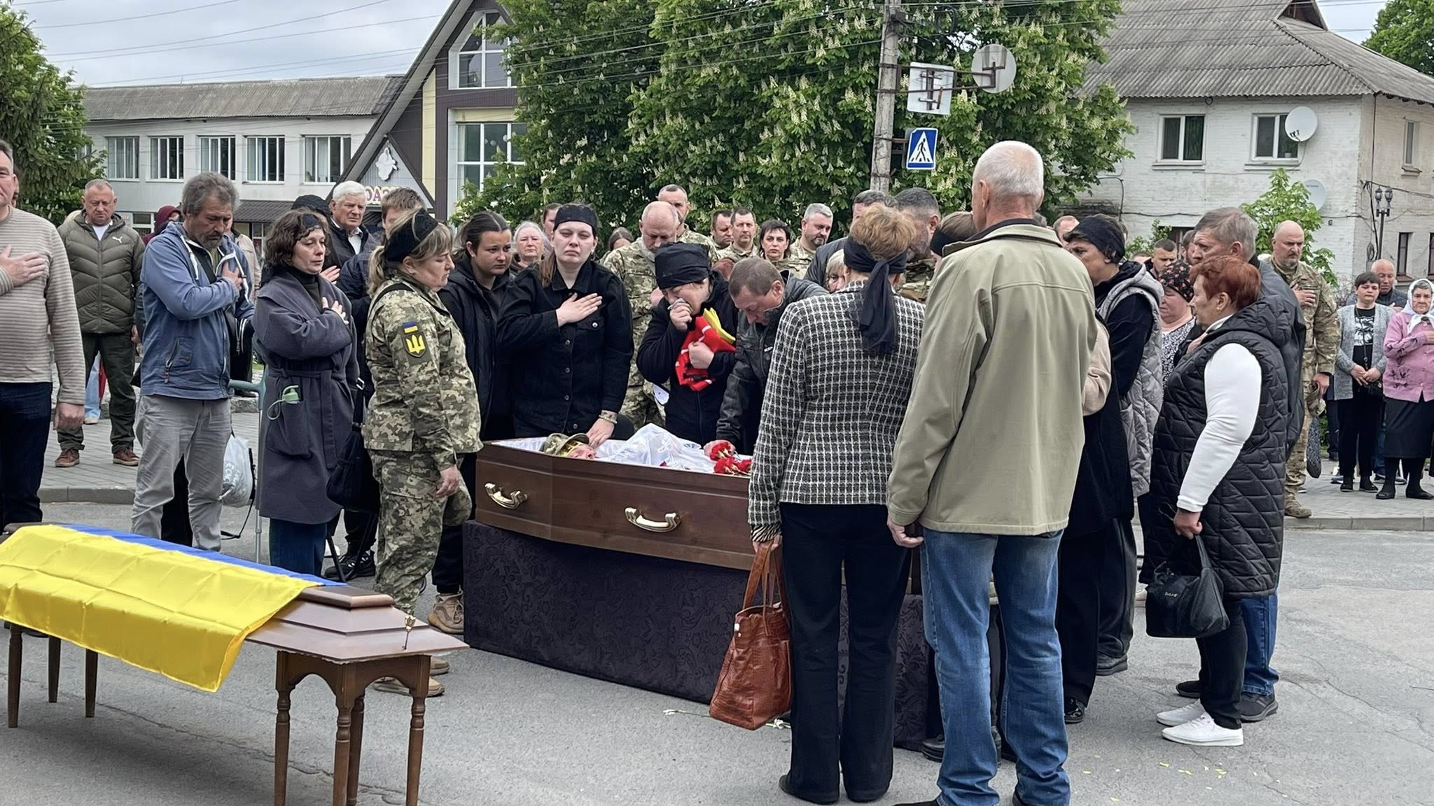 Mourners gather around a casket with yellow flowers at a street funeral procession.