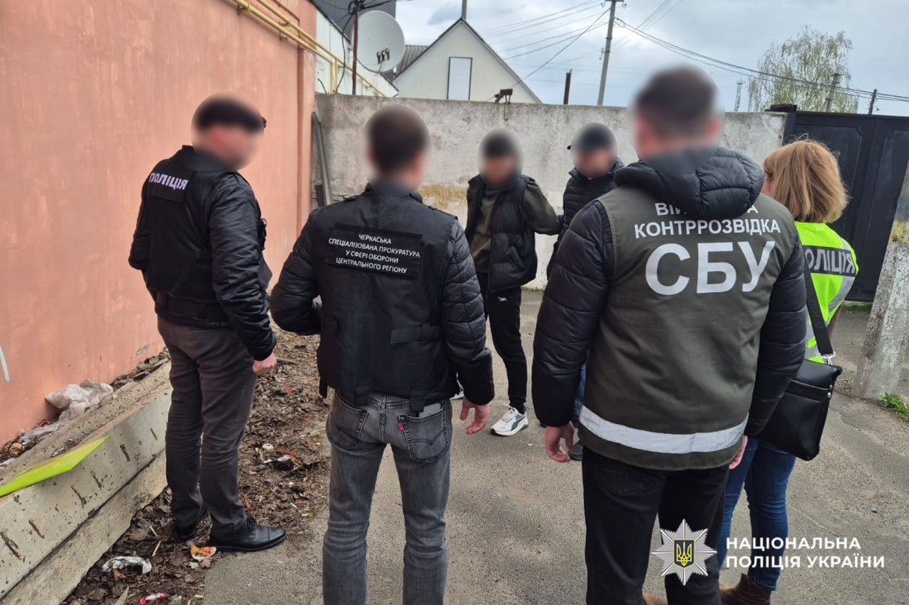 Group of Ukrainian police and SBU counterintelligence officers talking in an alley, back to camera; jackets display SBU and National Police logos.