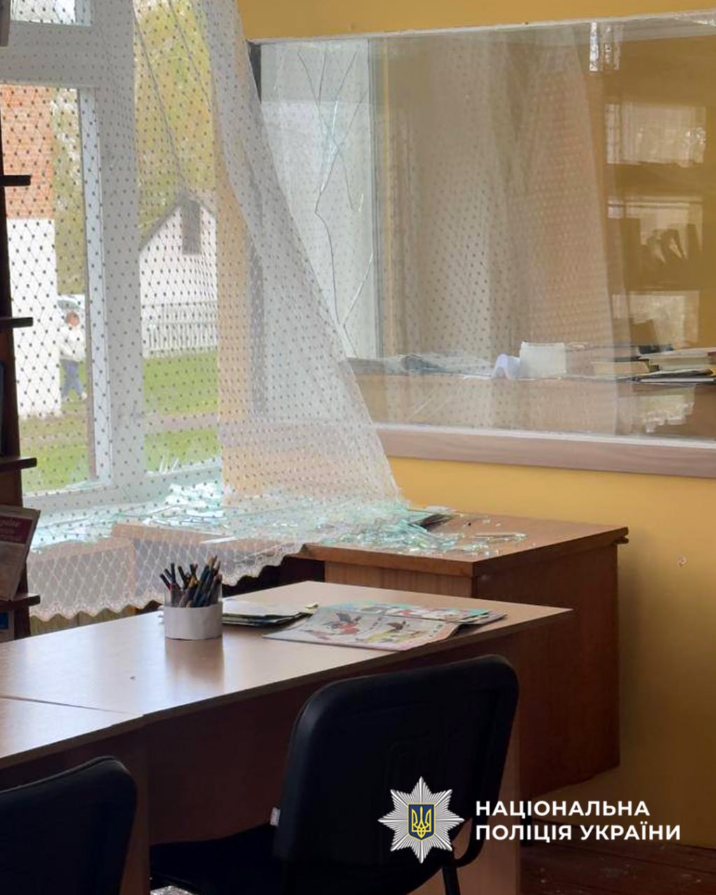 Office interior showing broken window glass and a translucent dotted curtain, with papers scattered on desks (police watermark visible).