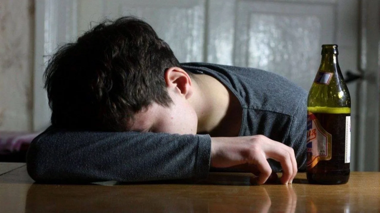 Person resting his head on a table with a beer bottle to the side, suggesting exhaustion or sadness.