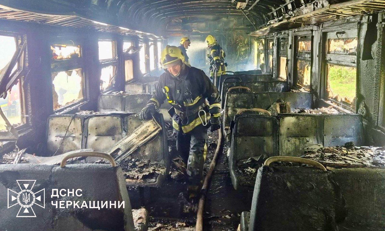 Firefighters in full gear moving through a burned-out bus interior, hoses on the floor and charred seats; emergency operation underway.
