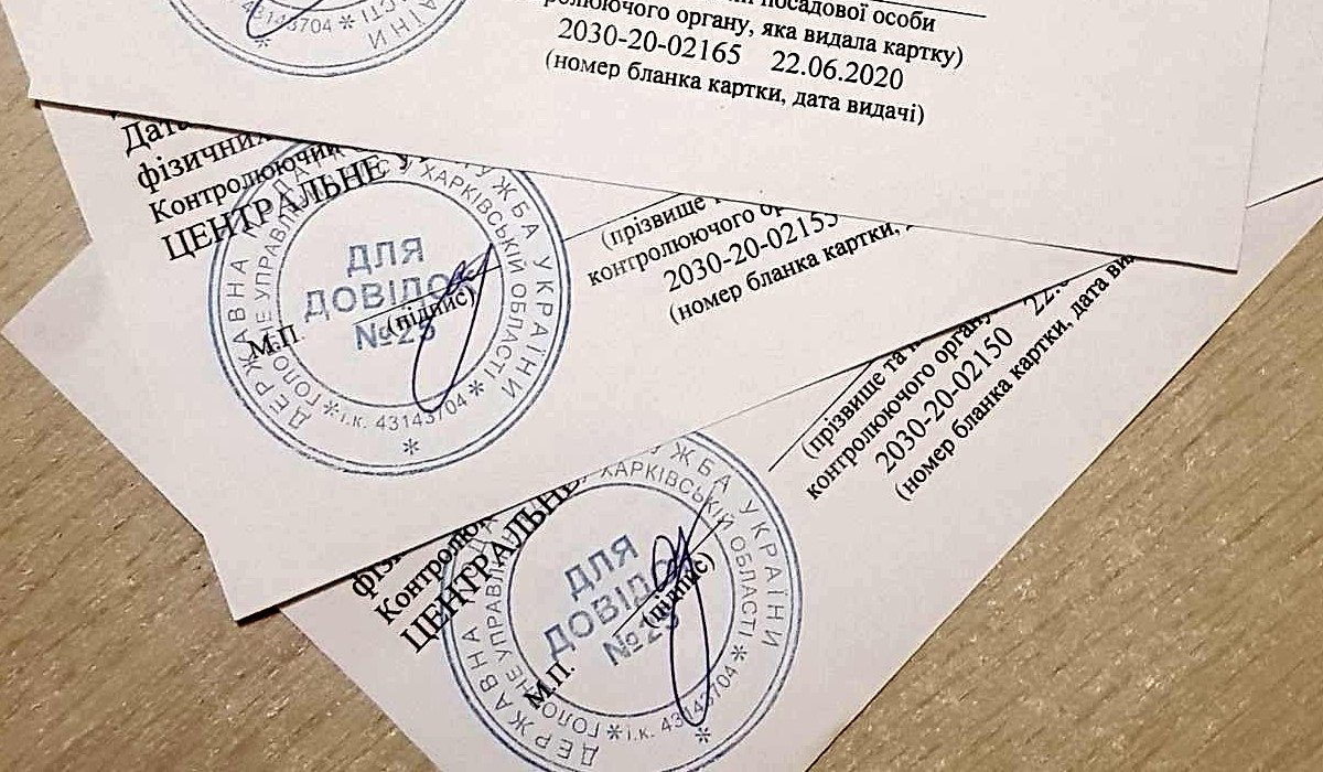 Several white official cards with blue circular stamps and signatures overlapping on a wooden desk surface.