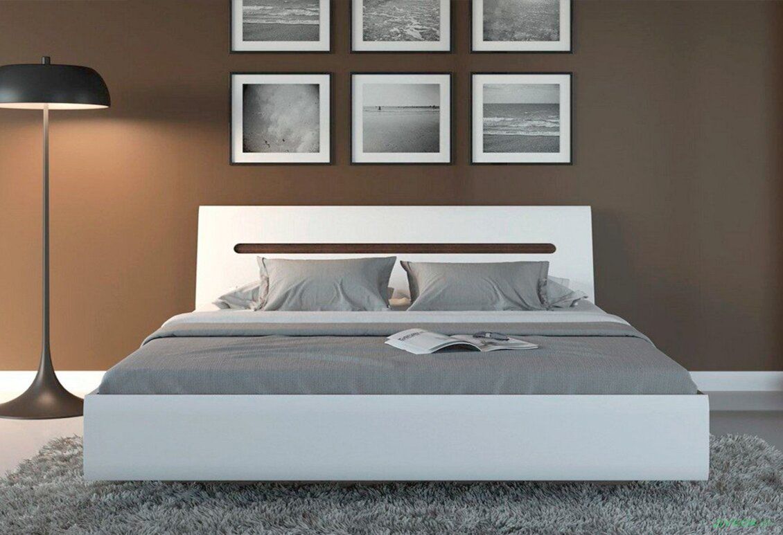 Modern white platform bed with gray bedding and a black floor lamp on a brown wall, six framed black-and-white photos above the headboard, fluffy gray rug nearby.